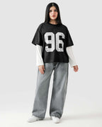 Person wearing a black oversized t-shirt with '96' printed on it, white long-sleeve shirt underneath, gray jeans, and white sneakers.